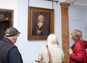 Three people looking at a portrait painting of Matthew Boulton hanging on the wall