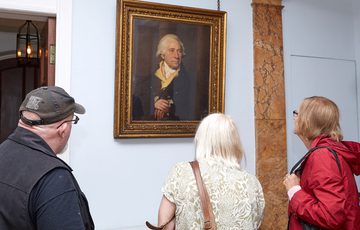 Three people looking at a portrait painting of Matthew Boulton hanging on the wall