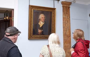 Three people inside Soho House looking at a portrait of Matthew Boulton that hangs on the wall