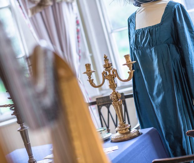 Closeup of part of harp with ladies blue Georgian dress in background.