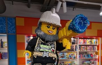 A large figure made out of lego is standing on a dispaly unit with many different boxes of lego for sale.