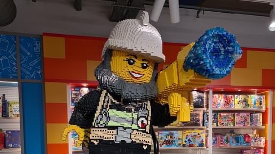 A large figure made out of lego is standing on a dispaly unit with many different boxes of lego for sale.