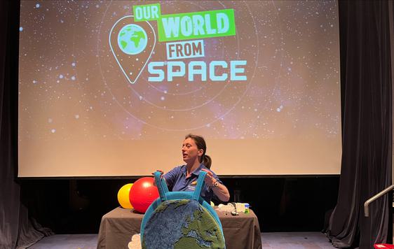 A Learning Officer holding a planet earth outfit while performing a show with screen in background that ready 'Our World From Space'.