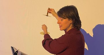 A staff member sitting while reading a booking and holding a musical instrument.