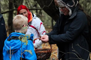 An adult holding a fungi and showing a group of people, they are outside in a woodland.
