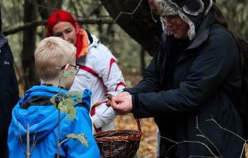 An adult holding a fungi and showing a group of people, they are outside in a woodland.