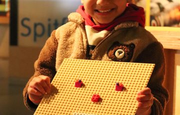 A child holding a LEGO baseplate with a face designed on it.