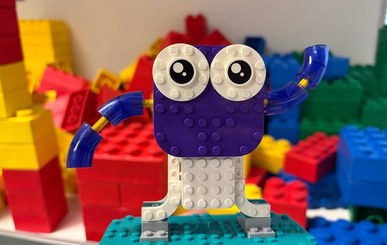 A LEGO figure with eyes and arm, with bricks in the background.