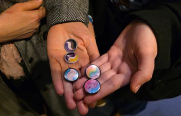 Two hands holding a group of colourful pride marble-style badges.