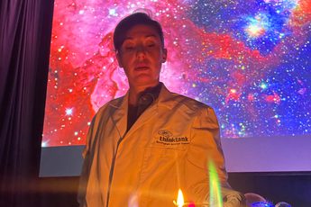 A staff member in a lab coat doing a science experiment with bright colour flames on a table in front of them.