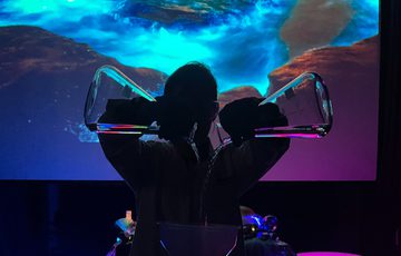 A silohette of a person pouring two tubes into a bowl of glowing liquid.