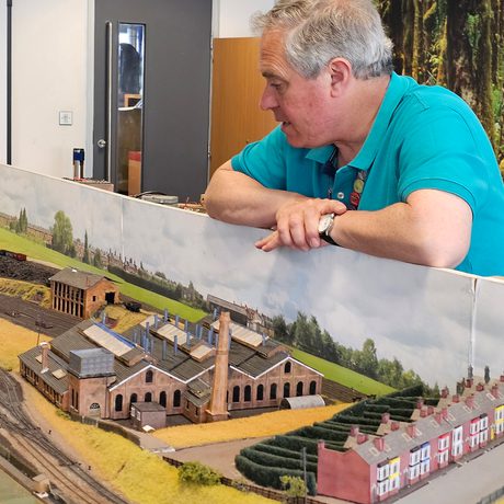 A person looking at a model railway with a track and buildings.