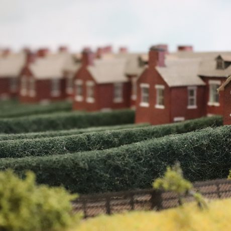 A close up model houses and gardens on a railway track.