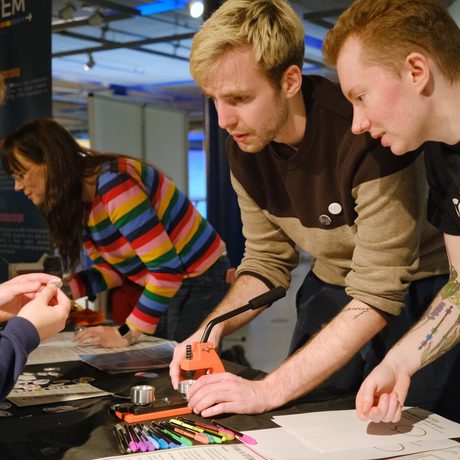 Two people assist a child with a hands-on STEM project while another person works nearby.