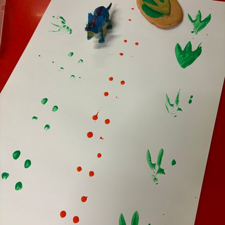 Toy dinosaur footprints in paint on paper.