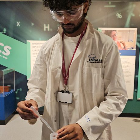 A staff member wearing googles and lab coat putting a liquid into a canister.