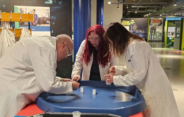 A group of three people wearing lab coats leaning over table with small canisters.