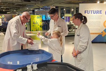 A group of three adults and a child wearing lab coats getting a canister out of a plastic box.