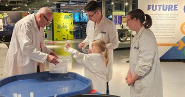 A group of three adults and a child wearing lab coats getting a canister out of a plastic box.