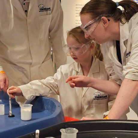 And adult and a child wearing lab coats putting liquid into a canister.