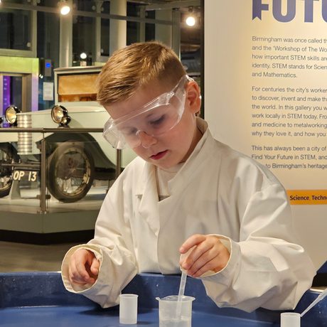 A child wearing a lab coat taking liquid from a canister.