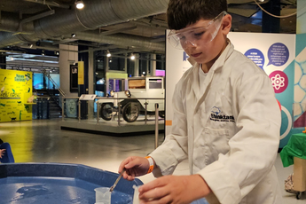 A child wearing lab coat putting liquid into a canister.