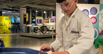 A child wearing lab coat putting liquid into a canister.