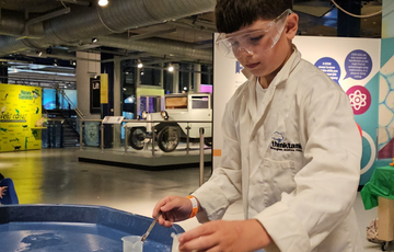 A child wearing lab coat putting liquid into a canister.