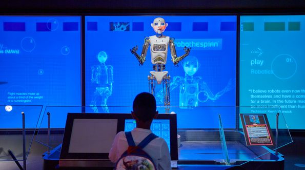 A robot is standing in front of a boy. The robot appears to be talking or singing.