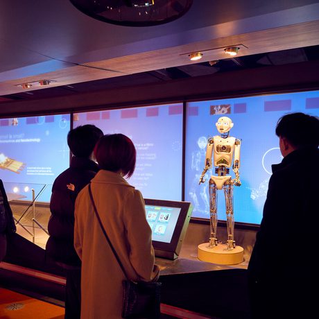 People observe a humanoid robot displayed in a dimly lit, modern exhibition space.