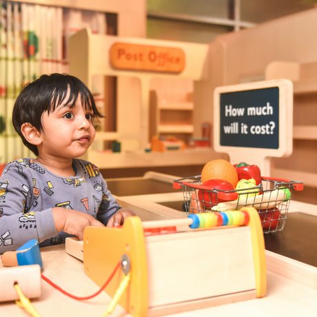 Child sitting at a play till with a basket of groceries.