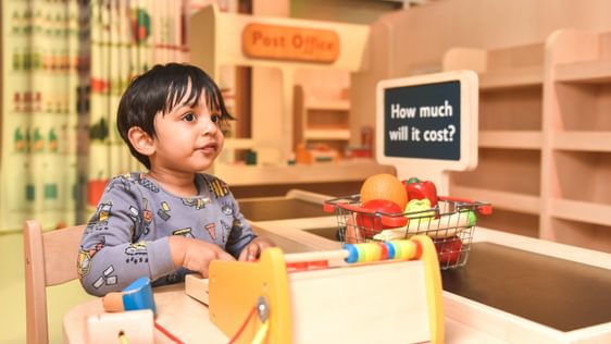 Child sitting at a play till with a basket of groceries.