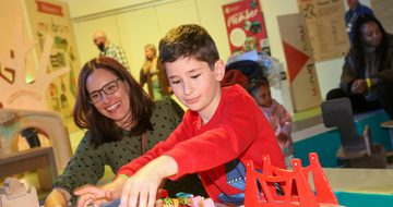 An adult and a child playing with a wooden toy train set.