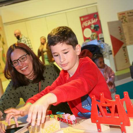 An adult and a child playing with a wooden toy train set.