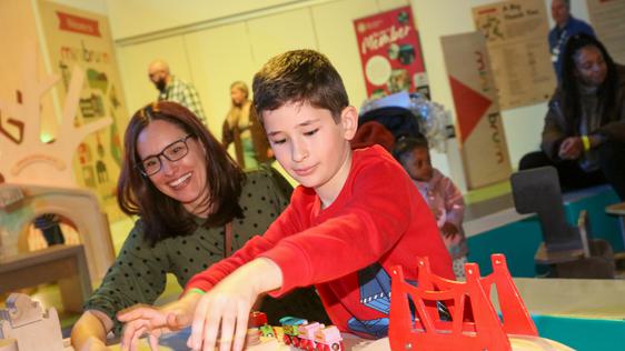 An adult and a child playing with a wooden toy train set.