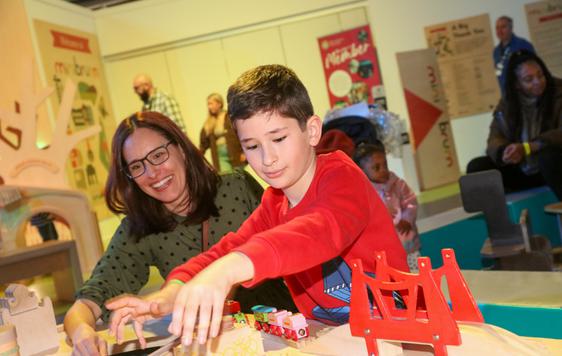 An adult and a child playing with a wooden toy train set.