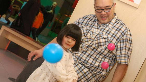 An adult with a child looking at the small plastic balls floating in the air.