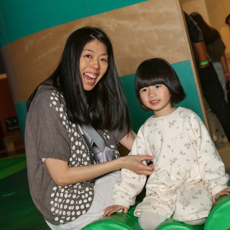 A adult and child smiling while sitting on the side of a soft play area.