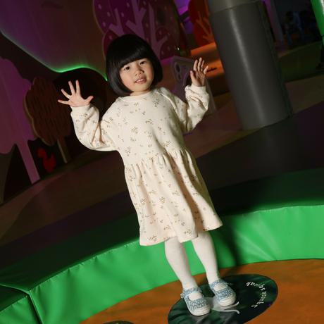 A young child with her hands in the air standing on a circle within a soft play area.