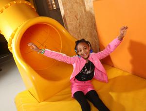 A girl smiling with her hands in the air sitting at the end of a slide.