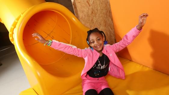 A girl smiling with her hands in the air sitting at the end of a slide.