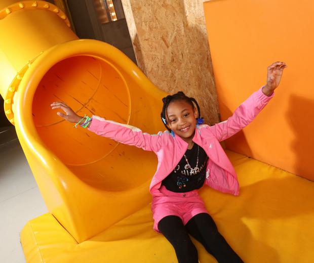 A girl smiling with her hands in the air sitting at the end of a slide.