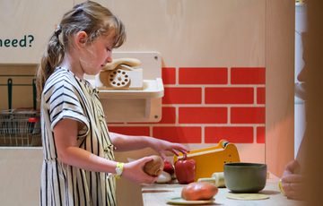 Young girl playing with toy kitchen utensils, arranging vegetables and food items.