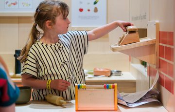 Girl adjusting colourful shapes on wooden face-shaped wall activity panels.