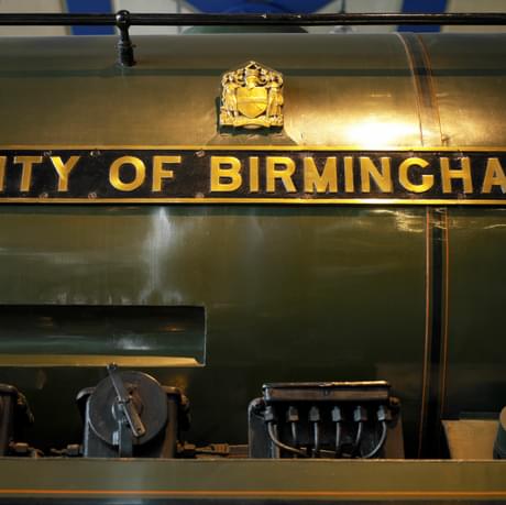 Close up of a name badge on a green train. City of Birmingham is written in gold lettering on a black background.