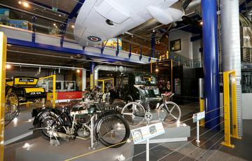 Exhibition hall with vintage motorcyles, cars and other bikes. A Spitfire plane is hanging above.