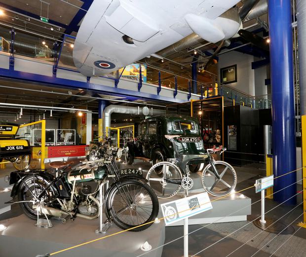 Exhibition hall with vintage motorcyles, cars and other bikes. A Spitfire plane is hanging above.