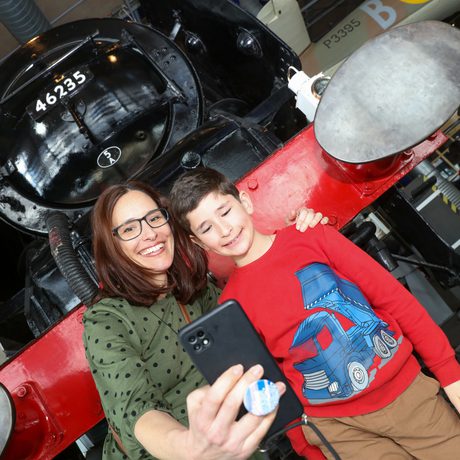 An adult and child taking a selfie in front of the steam train.
