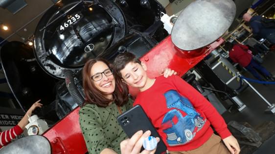 An adult and child taking a selfie in front of the steam train.