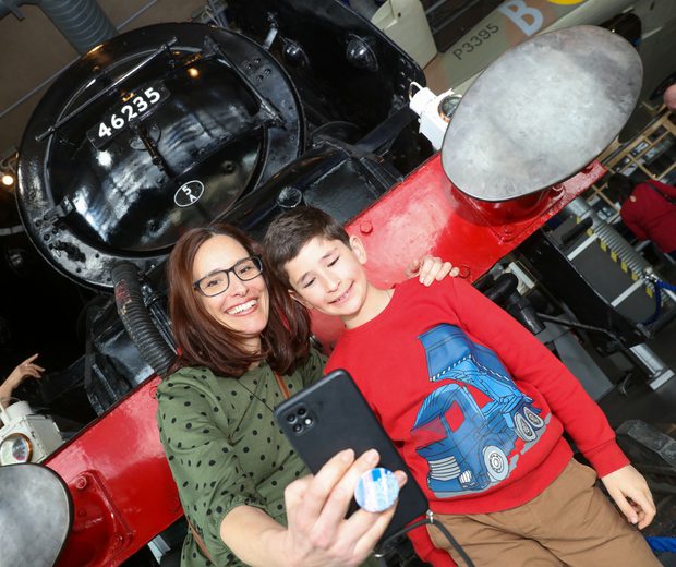 An adult and child taking a selfie in front of the steam train.